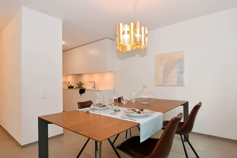 Dining room with a wooden table, four brown leather chairs, white tablecloth, wine glasses, plates, forks, knives, a bottle, and a chandelier
