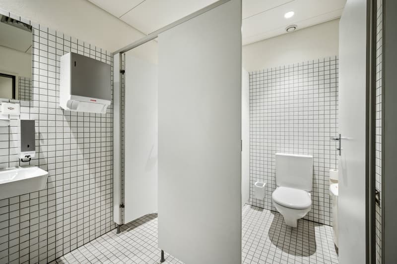 Tiled bathroom with white walls and floors, toilet, sink, and washing machine