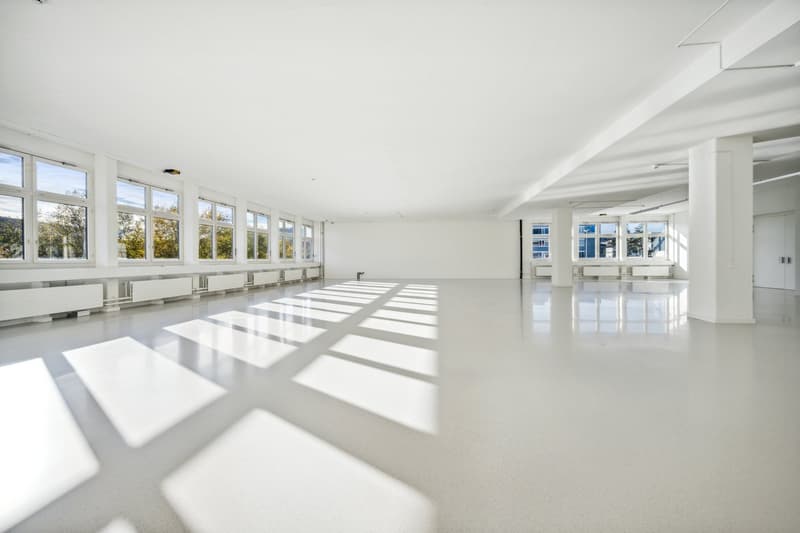 Large open-plan office space with high ceilings, large windows providing ample natural light, and a polished concrete floor. The room appears to be empty, ready for use as a commercial or office space.