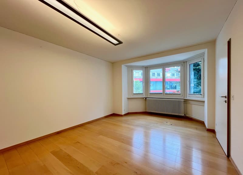 Spacious room with hardwood flooring, large windows providing natural light, and a modern lighting fixture on the ceiling.