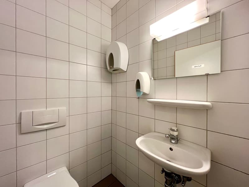 Tiled bathroom with a sink, mirror, and toilet paper dispenser. The room has a clean, minimalist design.