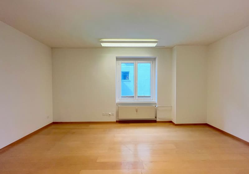 Empty room with hardwood flooring, white walls, and a large window. The room appears to be a living room or bedroom with a simple, minimalist design.