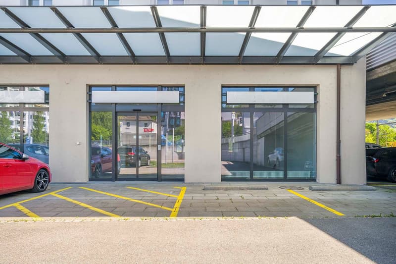 Modern building with glass doors and windows, a red car parked in front, and a parking area with yellow markings.
