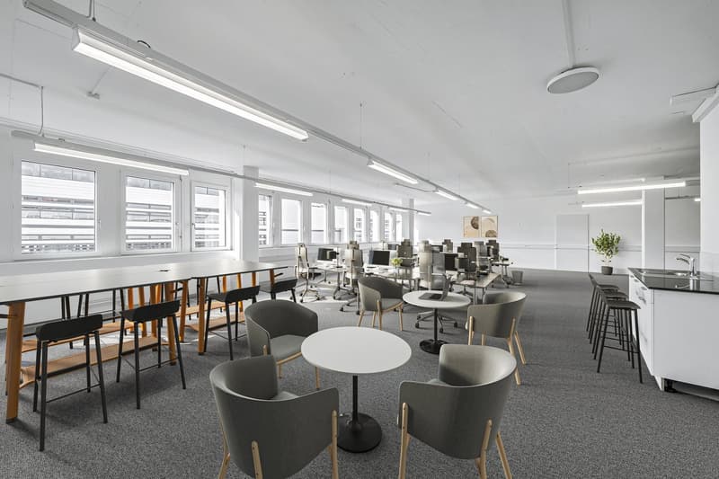 modern office space with desks, chairs, tables, and a kitchen area