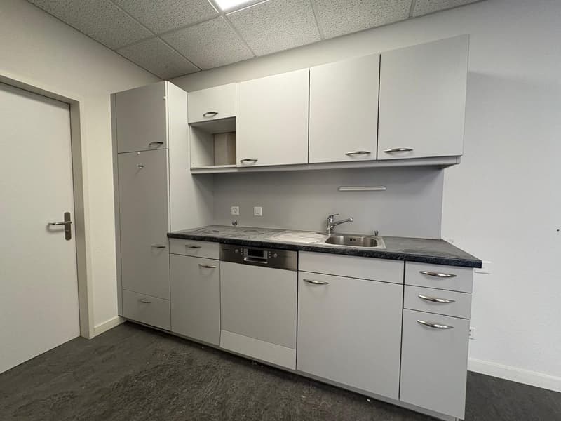 Compact kitchen with white cabinets, granite countertop, built-in dishwasher, and sink