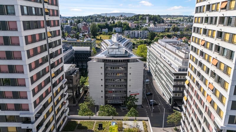 Aerial view of a city skyline with high-rise buildings, residential apartments, and commercial structures. The image shows a mix of modern and older architectural styles, with some buildings having balconies or terraces visible.