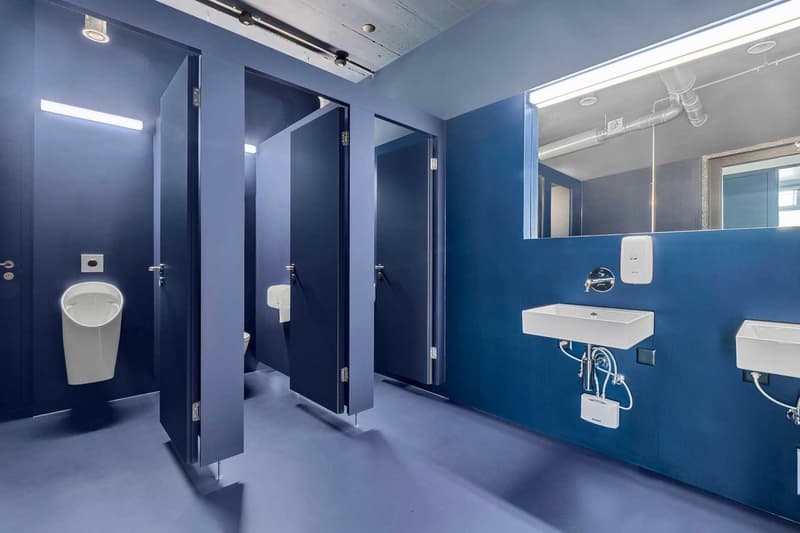 Large bathroom with blue walls, multiple stalls, urinals, and a sink vanity