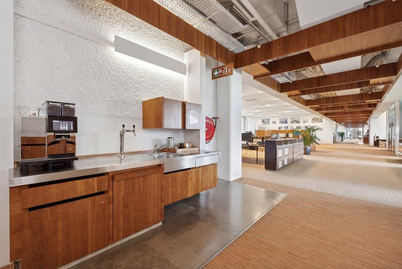 Modern kitchen with wooden cabinets, stainless steel appliances, an island sink, and a red fire extinguisher mounted on the wall.