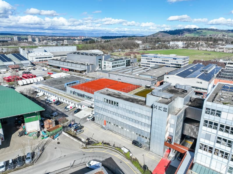 Industrial buildings with parking lots, solar panels on roofs, a red tennis court, multiple buildings, and surrounding area