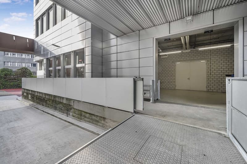 Commercial building, metallic panels, multiple windows, open parking garage, paved area