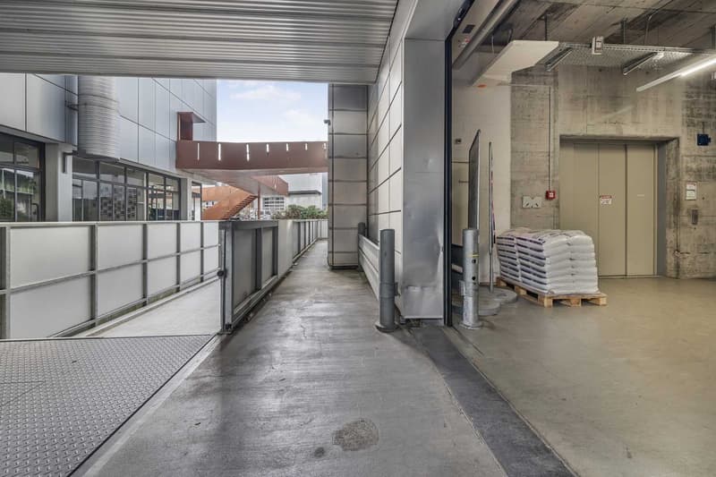 Empty garage with cement floor, entrance gate, metal barriers, metal panels on the wall, and an open door.