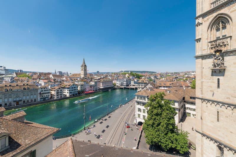 Aerial view of city buildings, a river, pedestrians, and a clock tower