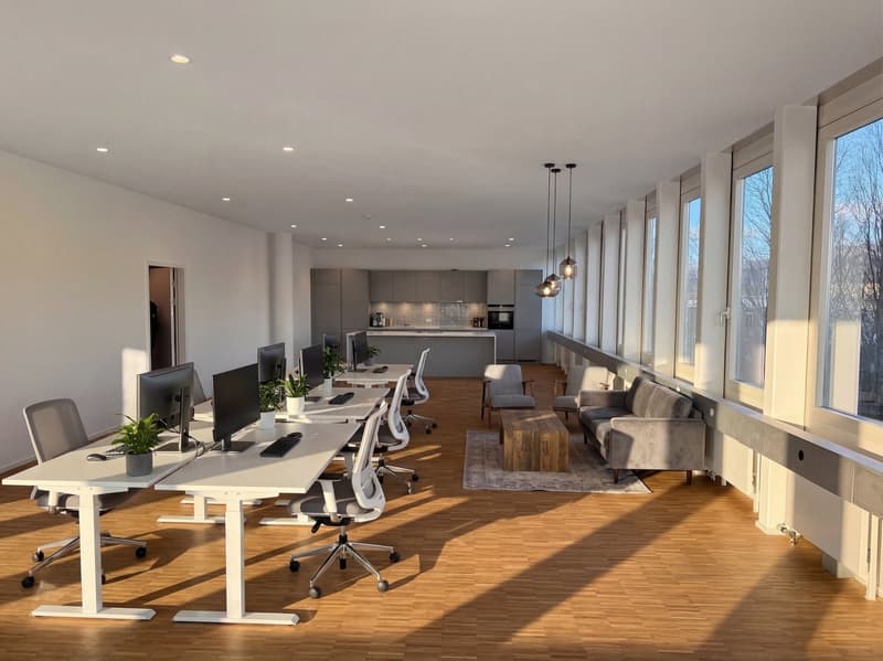 modern office space with white desks, ergonomic chairs, multiple computer monitors, wooden coffee table, gray couches, large windows