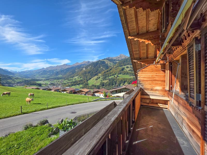 Mountain view, wooden balcony, valley, cows grazing, distant houses