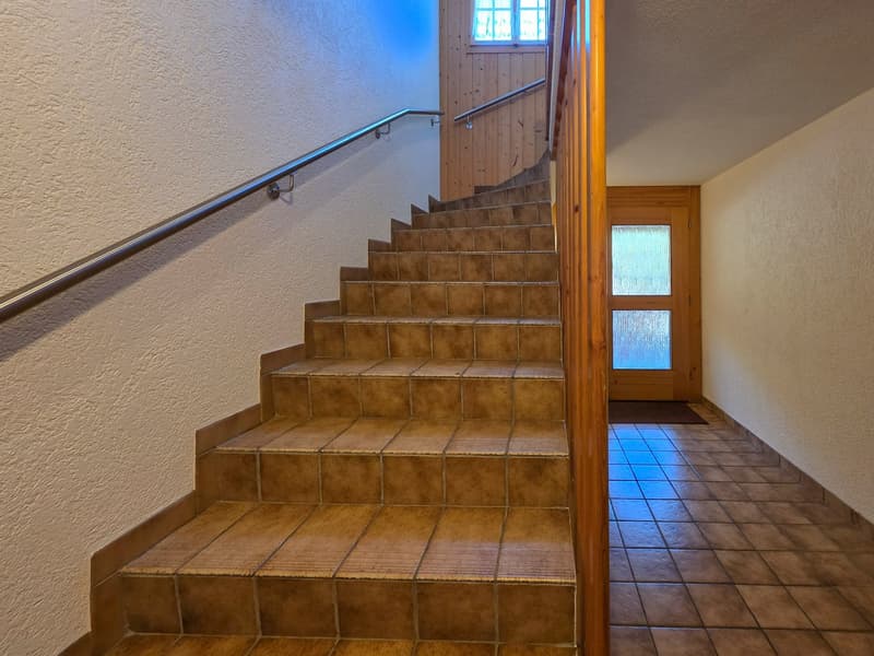 A tiled staircase, a wall with a window and door, and a wooden railing.