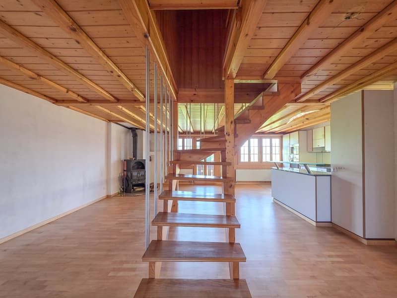 Large open room with wooden staircase, wooden flooring, white walls, wooden ceiling, fireplace, kitchen with countertops