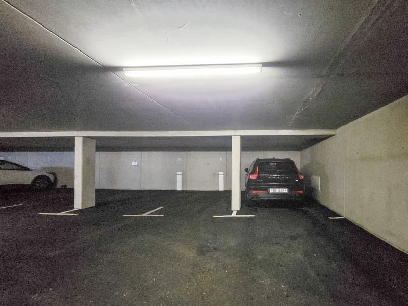 underground parking lot, two cars parked, white walls, white ceiling, white lights