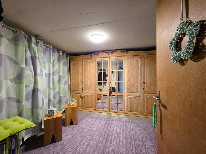 A room with a wooden wardrobe, a wooden stool, a green cushion, a tissue box, a glass bowl, a white ceiling, and a green wreath on the door.