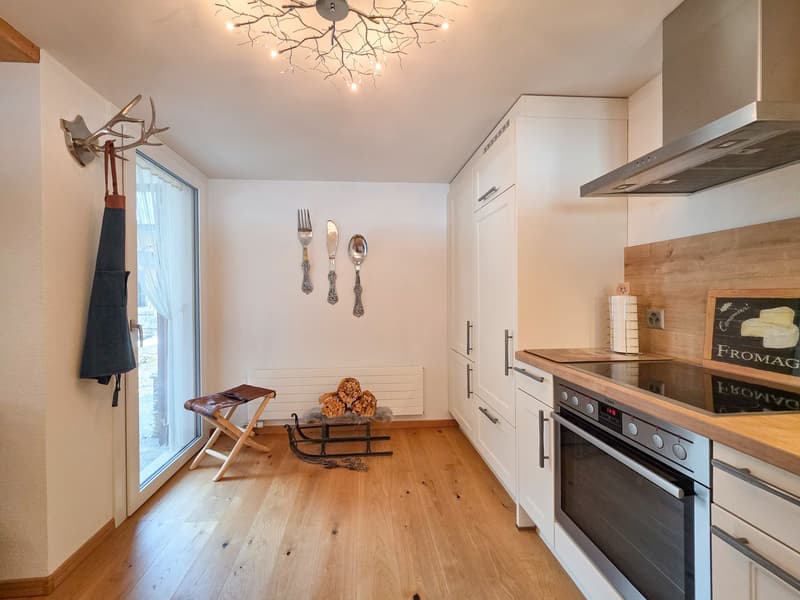 modern kitchen with wooden floor, white cabinets, wooden countertop, stainless steel appliances, chandelier, glass door, wooden stool, firewood