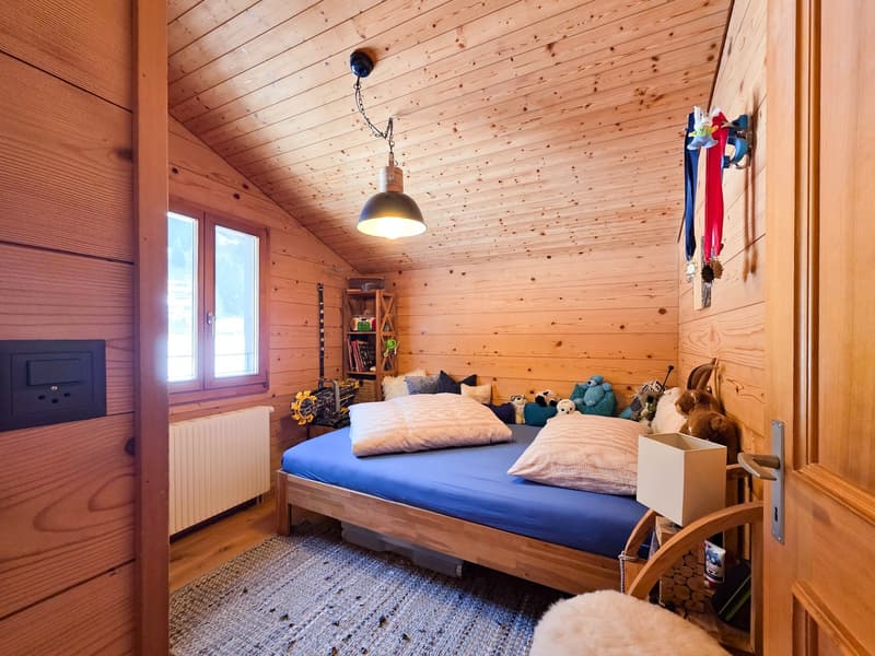 wooden walls, wooden bed, blue sheets, pillows, lamp, radiator, window, rug, toys, shelf