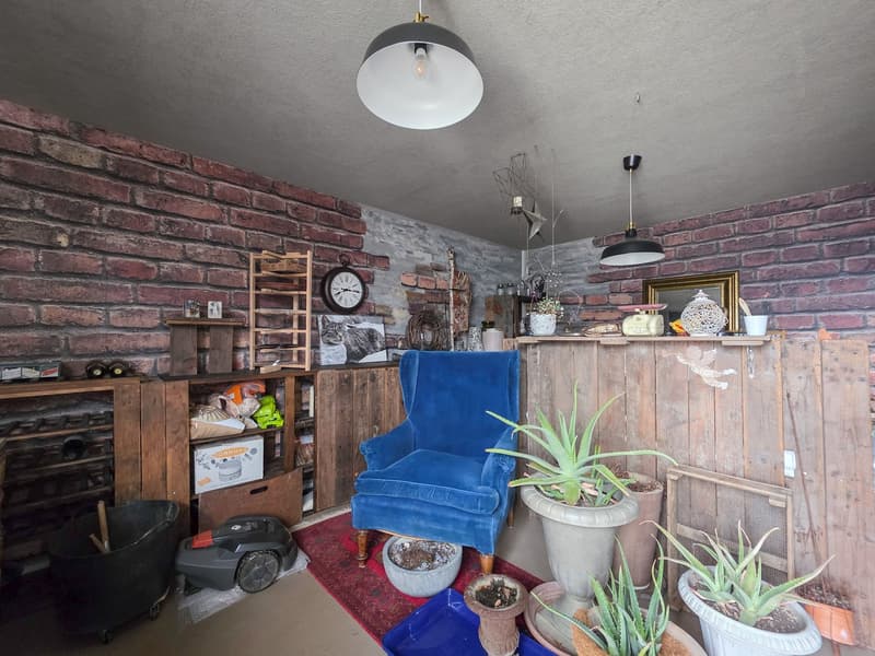 brick wall, wooden furniture, blue armchair, potted plants, wooden shelves, clock, mirror, lamps