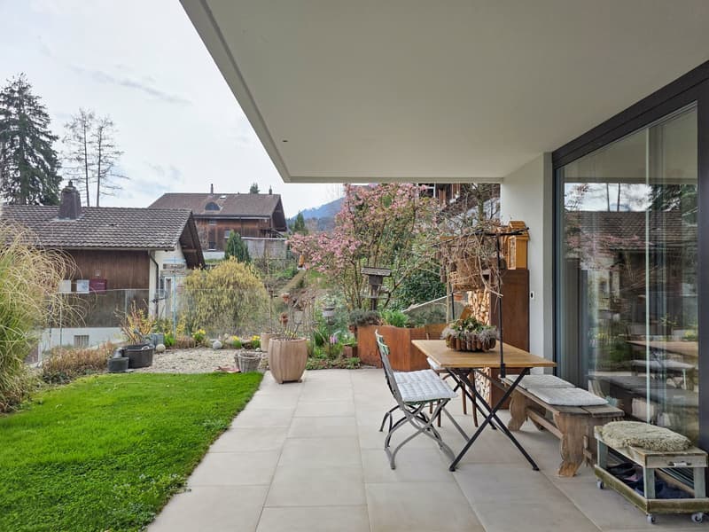 Terrace with table, chairs, bench, and potted plants, green lawn, and garden area with various plants and trees
