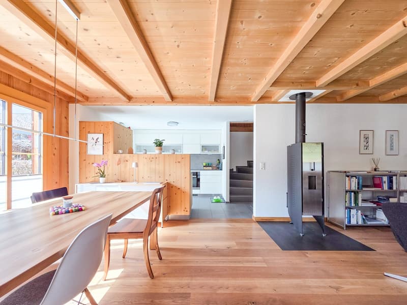 dining room with wooden table, chairs, wooden beams, fireplace, kitchen, staircase, bookshelves, picture frames
