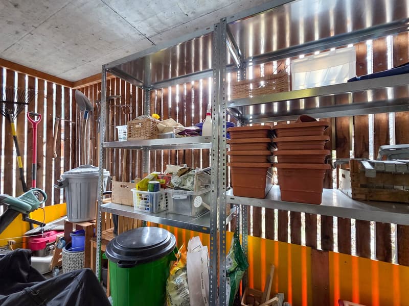 Storage room with metal shelves, storage boxes, gardening tools, trash bins, and various items
