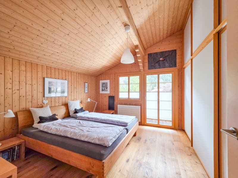bedroom with two single beds, wooden walls, wooden floor, lamps, nightstands, picture frames, sliding glass door, radiator