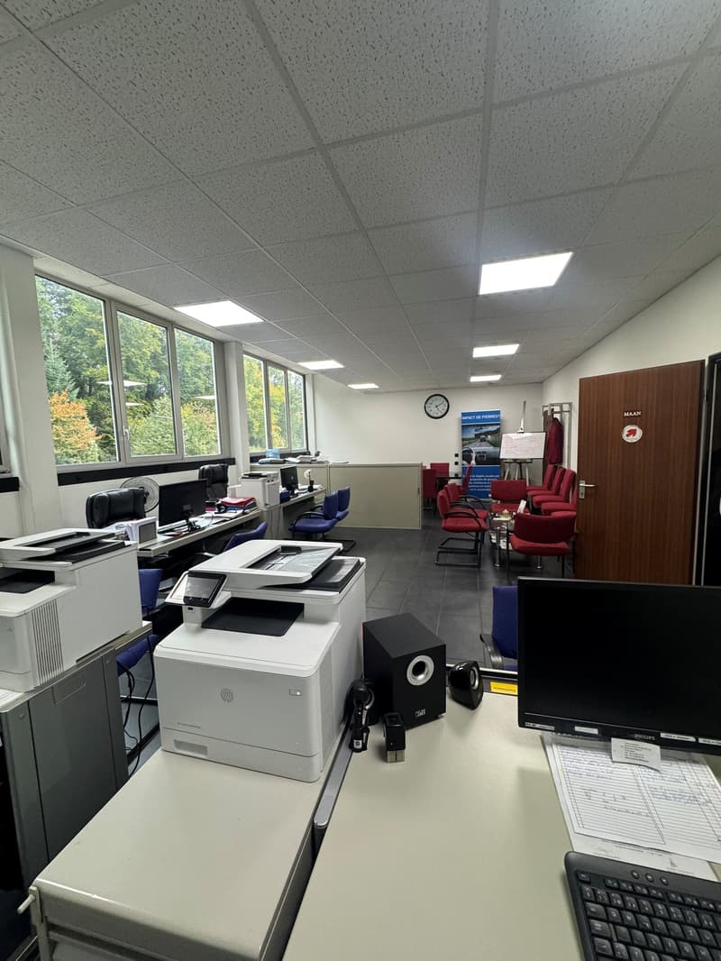 large office space with white walls, tiled floor, multiple computers and printers, desks and chairs