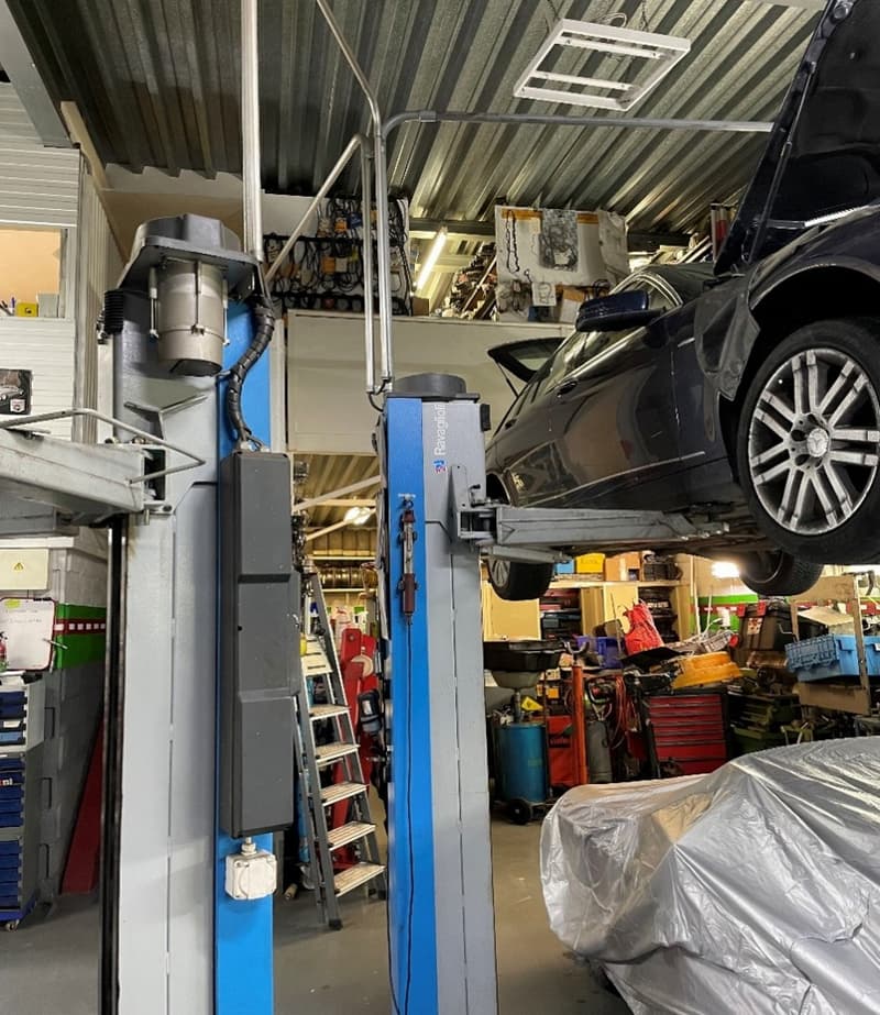 large metal rack system to lift cars, car in the middle, ladder against the wall, shelves with tools and equipment, car underneath a cover
