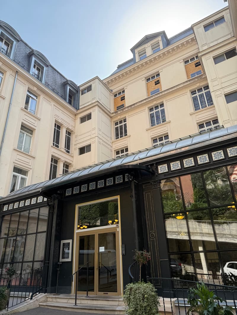 5 story building, black glass windows, metal frame on top, entrance door, small plants