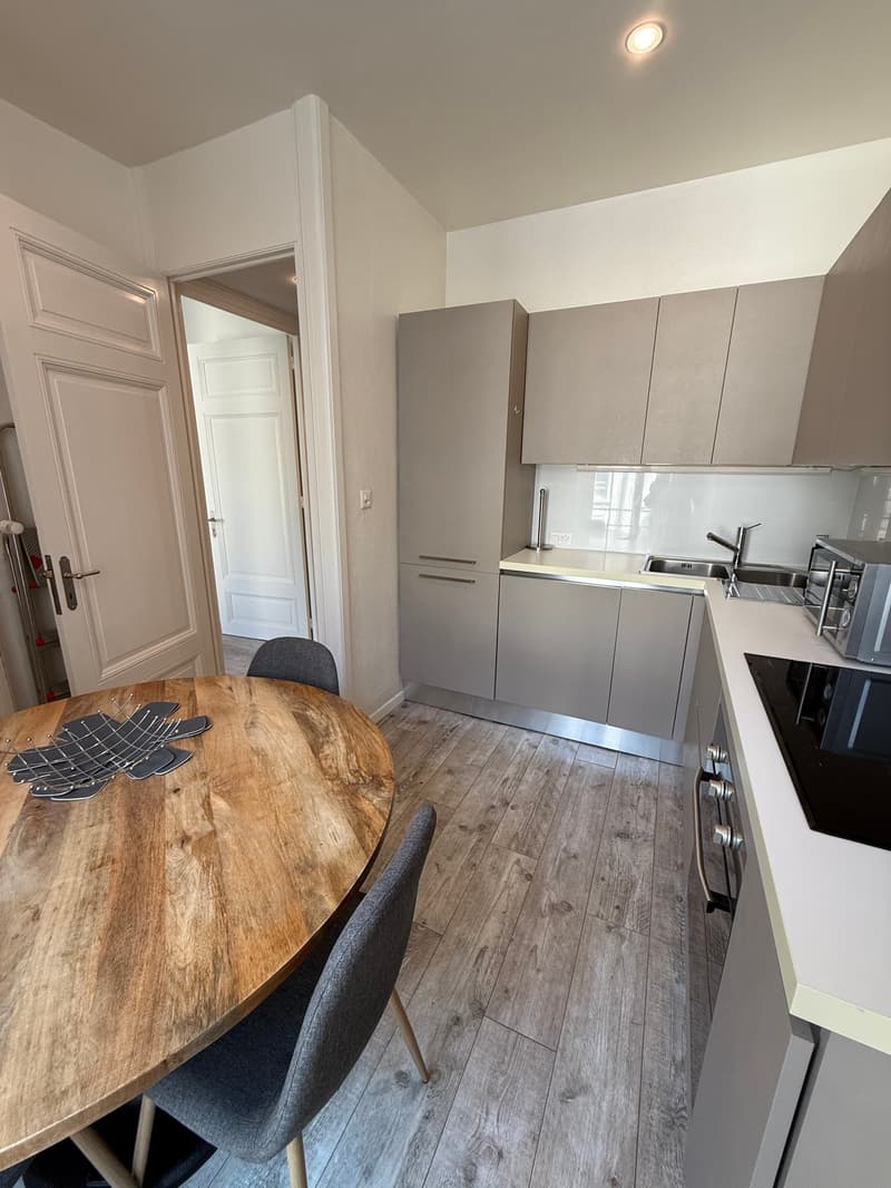 round wooden table, 2 gray chairs, gray cabinetry, white countertops, black stovetop, stainless steel faucet, sink, microwave