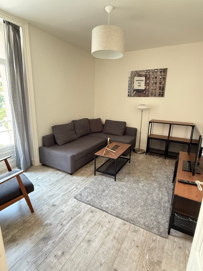 modern style living room, beige floor, gray couch, wooden coffee table, wooden chair, large windows with gray curtains, floor lamp, artwork, wooden TV stand, flat screen TV, rug