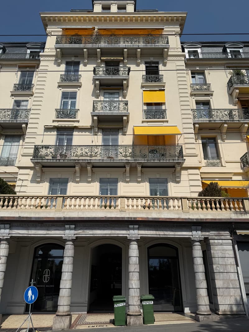Large building, multiple balconies, yellow awnings, stone columns, multiple floors