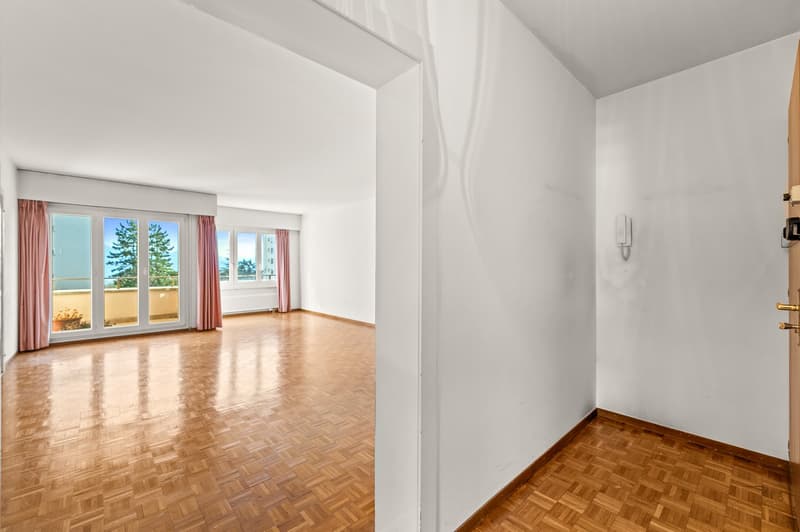 Empty room with wooden floor, large windows, pink curtains, telephone on the wall