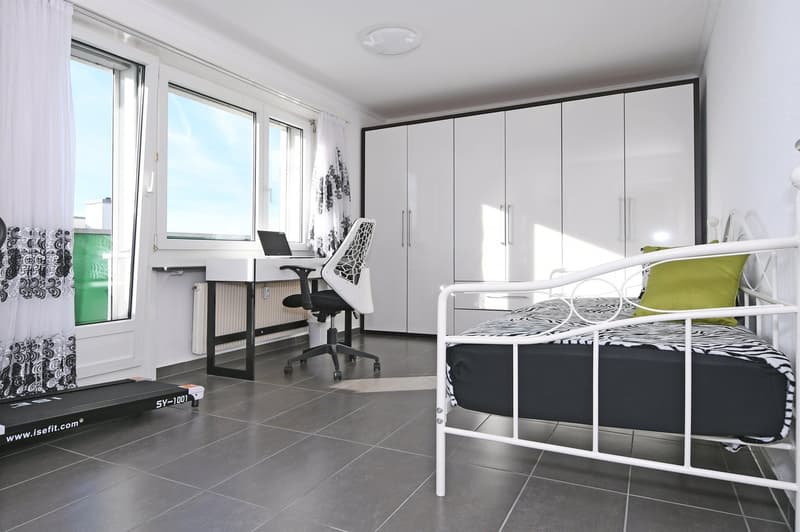 modern minimalist room with white walls, white bed, black and white zebra print bedsheet, white chair, white desk with laptop and radiator