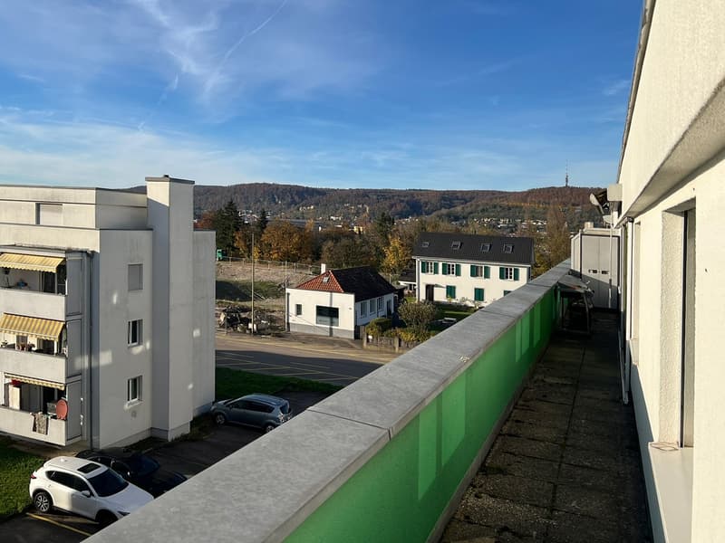 residential building, parking area with cars, green area, distant buildings, mountains