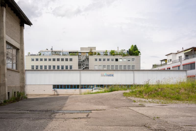 A multi-story commercial building with the Baminox logo displayed on the facade. The building has a modern, industrial design with large windows and a grassy area in the foreground.