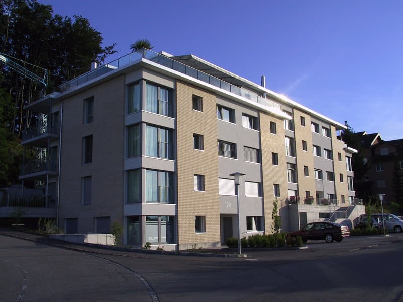 Modern residential building with balconies and terraces, brick and glass exterior, 5 floors, parking lot in front