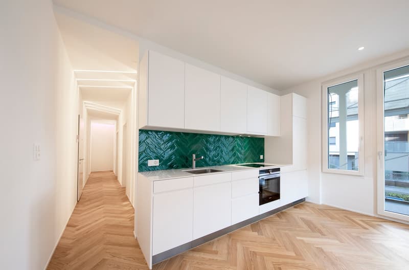 modern kitchen with white cabinets, green backsplash, wooden floor, stainless steel sink, faucet, oven, windows