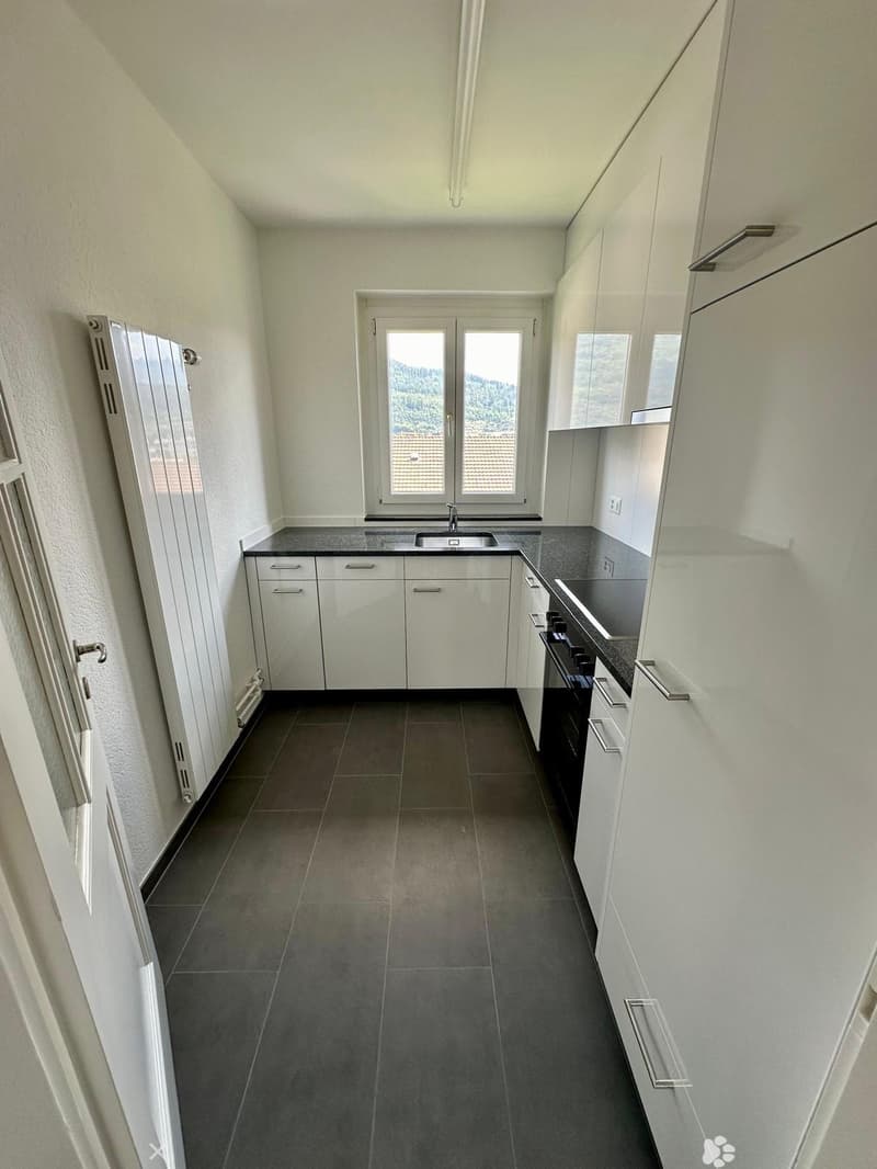 Modern kitchen with white cabinets, black countertops, tiled floor, stainless steel sink, integrated dishwasher, and an open window with a scenic view.