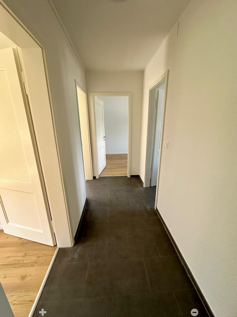 empty hallway, dark tiles, light walls, white doors, light wood flooring
