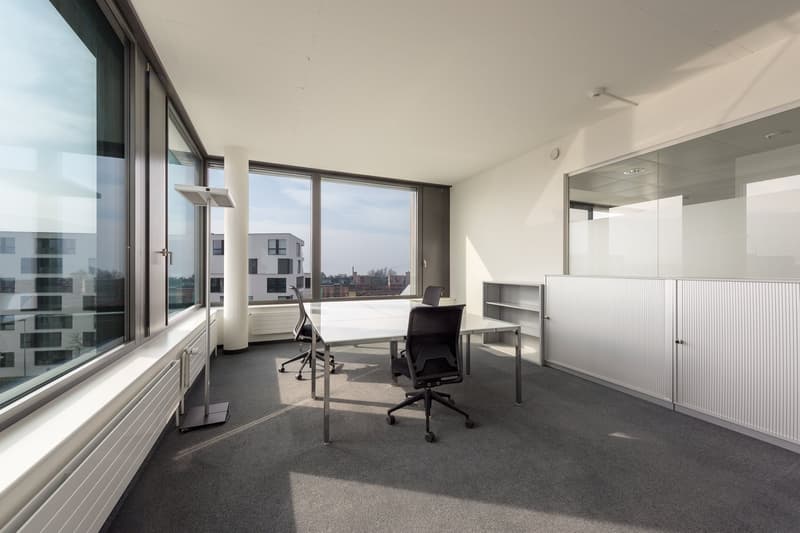 Spacious office with large windows providing a view of the city, modern furniture including desks and chairs, and built-in storage cabinets.