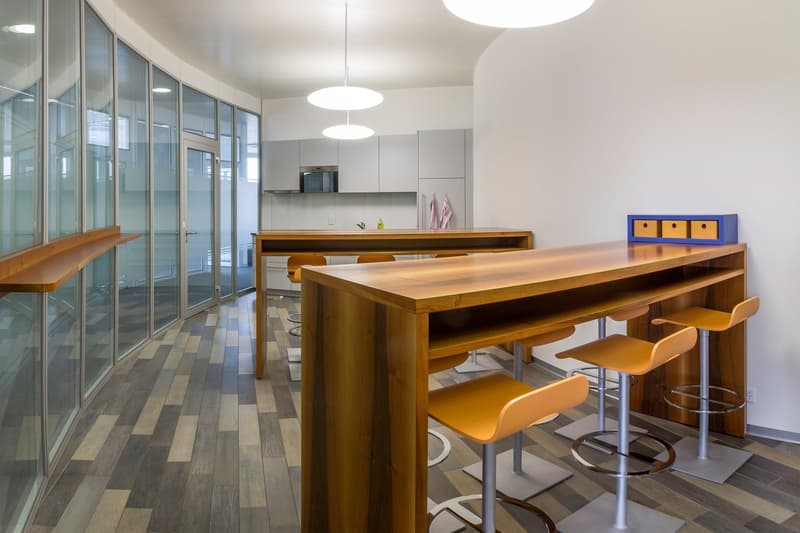 Modern kitchen with wooden countertops, bar seating, and glass walls providing natural light. The kitchen features a dishwasher and storage units.