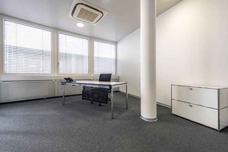 Spacious office with large windows, modern desk and chair, and a storage cabinet