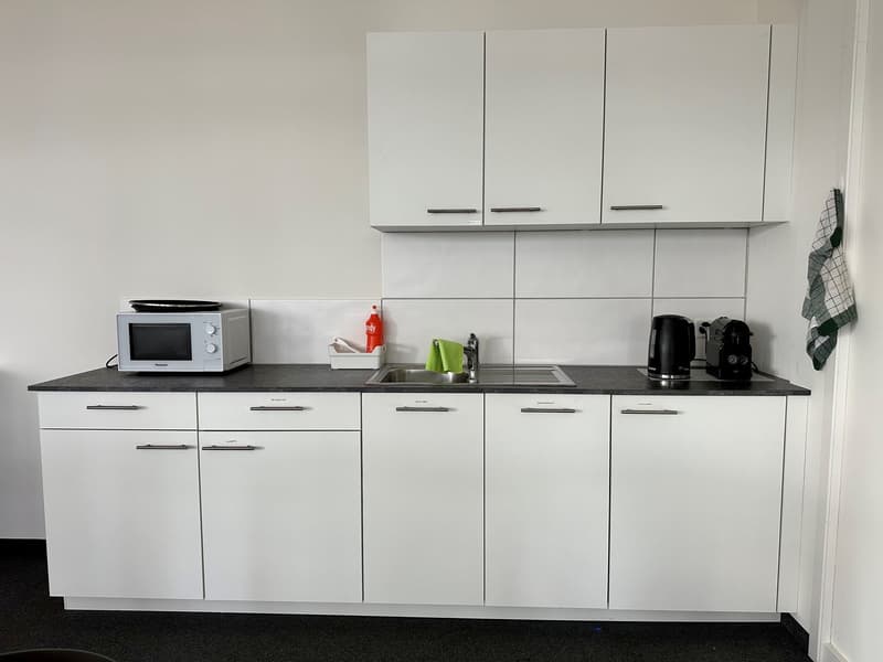 kitchen with a black countertop, white cabinets, microwave on the counter, sink, faucet, a kettle, dish soap and towels