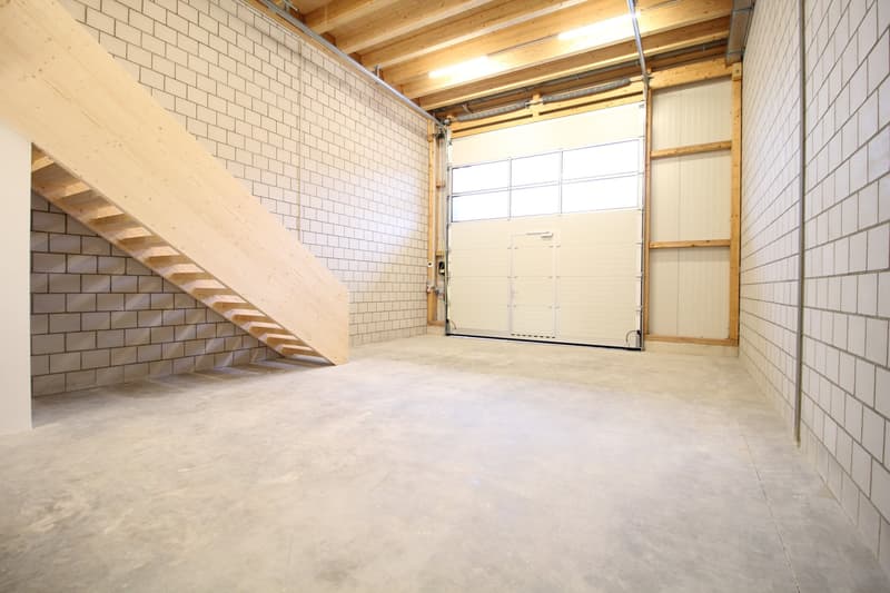 Empty room with white brick walls, wooden ceiling, concrete floor, wooden staircase, and a white garage door.