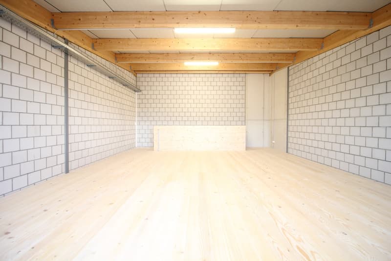 Large open room, wooden floor, white brick walls, wooden beams on the ceiling, recessed lighting