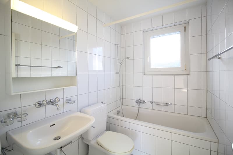 Bathroom with white tiles, white sink, white toilet, bathtub, shower, mirror, and window.